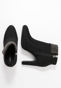 Botines de ante negros con punta afilada, tacón alto y cierre de cremallera adornado con una hilera de remaches decorativos en el puño.