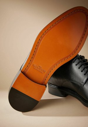 Schwarzer Lederschuh mit strukturiertem Obermaterial, kontrastierender brauner Ledersohle und schwarzem Absatz. Verfügt über sichtbare Nähte und ein Logo auf der Innensohle.