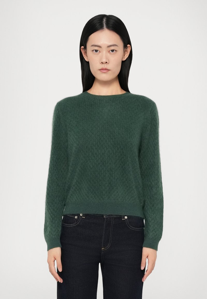 Groene gebreide trui met een textuurpatroon, ronde halslijn en lange mouwen, gecombineerd met een donkere jeans. Zacht, lichtgewicht materiaal.