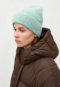 Gorro de punto azul claro con textura acanalada, combinado con una chaqueta acolchada marrón oscuro que presenta un cuello alto y un diseño de acolchado.