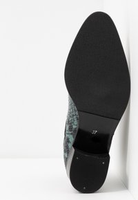 Semelle d'une chaussure à bout pointu avec semelle et talon noirs texturés, présentant un motif peau de serpent vert et noir sur le dessus, taille 37 marquée.