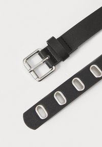 Schwarzer Ledergürtel mit silberner Metallschnalle, der entlang des Riemens große ovale Öffnungen aufweist. Glatte Textur mit einem minimalistischen Design.