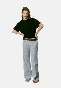 T-shirt noir à manches courtes associé à un pantalon large rayé gris et blanc. La tenue comprend une ceinture marron avec une boucle ronde.