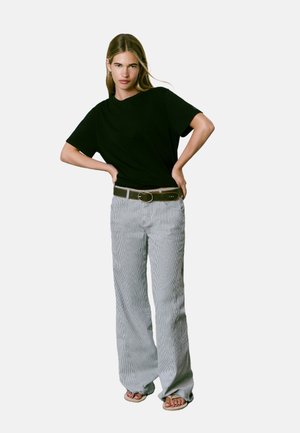 T-shirt noir à manches courtes associé à un pantalon large rayé gris et blanc. La tenue comprend une ceinture marron avec une boucle ronde.
