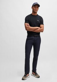 Svart t-shirt med kort ärm och logotyp, marinblå byxor, svart skärp, och flerfärgade sneakers. Modellen bär en grå keps.