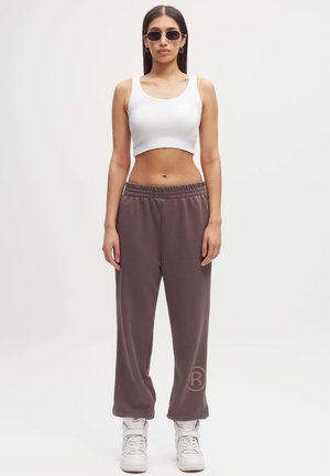 Biały prążkowany crop top i luźne, szaro-brązowe dresy z logo. Noszone z białymi wysokimi trampkami. Gładka faktura materiału.