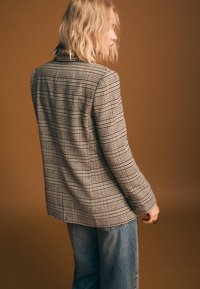 Blazer sartoriale a quadri in tonalità beige e nero, con un design strutturato e rever a incavo, abbinato a denim azzurro chiaro.