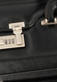 Black leather bag featuring a silver metallic lock mechanism and combination dials, with visible stitching and a smooth texture.