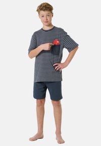 Tyrkysově modré a bílé pruhované tričko s krátkým rukávem a kapsou na prsou; v kombinaci se sněhobílými kraťasy. Model stojí naboso a ukazuje na kapsu.