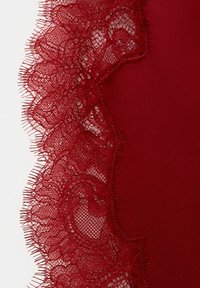 Tela de color rojo intenso con encaje floral intrincado que presenta bordes festoneados y detalles finos de hilo sobre un fondo sólido.