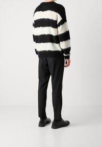 Czarnobiały, prążkowany, puszysty sweter o luźnym kroju, ze ściągaczami na mankietach i u dołu. W zestawie z czarnymi spodniami i czarnymi, sznurowanymi butami.
