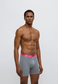 Γκρι μπόξερ σλιπ από απαλό ύφασμα με ροζ ελαστική μέση με το λογότυπο της Nike. Το σχέδιο έχει εφαρμοστή γραμμή και μήκος μέχρι τα μέσα του μηρού.