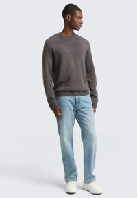 Grauer gestrickter Pullover mit rundem Halsausschnitt, gerippten Bündchen und Saum; kombiniert mit hellblauen, geraden Jeans und weißen Sneakers.
