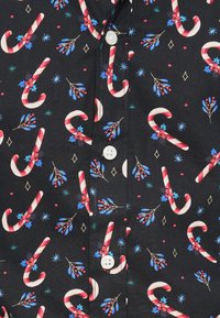 Svart stoff med et gjentatt mønster av røde og hvite julekuler, blå blader og blomster, med to hvite knapper ved halsen.