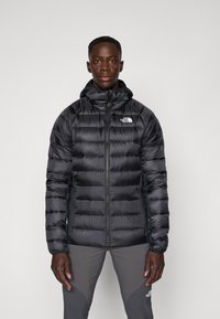 Schwarze Steppjacke mit Reißverschluss, Kapuze und dem North Face-Logo. Verfügt über gesteppten Abschnitte, eine glatte Textur und Seitentaschen.