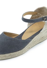 Sandal de cuña de lona gris con suela de yute, tira en el tobillo y plantilla acolchada. Presenta un diseño texturizado en la parte trasera para mayor detalle.