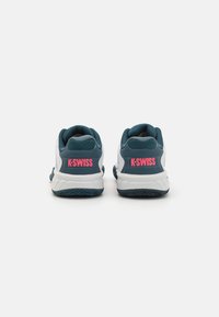 K-Swiss zolītes teal un baltā krāsā, ar tīkla augšdaļu, paaugstinātu mēli un rozā logotipu uz papēža. Riebgalvju gumijas zole labākai saķerei.
