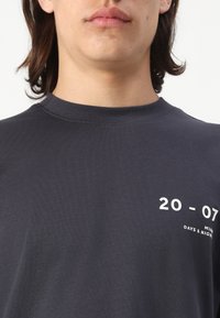 Mørk grå bomulls t-skjorte med korte ermer, ribbet rund hals og hvit grafisk trykk som inkluderer "20 - 07" og "MIAMI DAGER & NETTER."