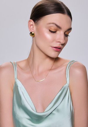 Złote kolczyki-wyrazy i delikatny złoty naszyjnik dopełniają jasnooliwkową satynową koszulkę na cienkich ramiączkach z drapowanym dekoltem.
