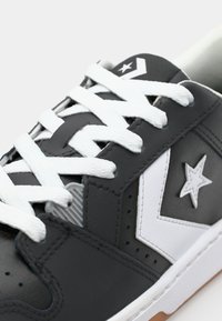 Gray sneaker featuring white laces, a leather upper, a star logo, and a rubber sole with a textured black accent.