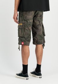 Kargo šorti ar kamuflāžas rakstu, izgatavoti no izturīgas auduma. Ar kabatām, auklām apakšmalā un sarkanu zīmola birku. Valkāti ar melnām zeķēm un sporta apaviem.