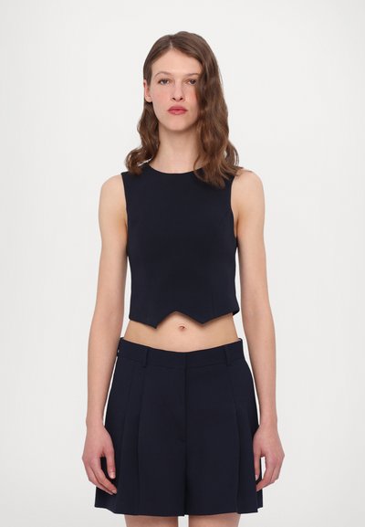 Námořnická modrá crop top s vlnitým lemem, vyrobená z hladké tkaniny. Spárovaná s námořnickými skládacími šortkami, které zdůrazňují přiléhavý siluetu.