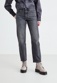 Pelēki denim džinsi ar taisnu kāju dizainu, augsta jostasvieta, piecas kabatas un diskrēti izšūšanas akcenti. Apvienoti ar bēšiem potīšu zābakiem.