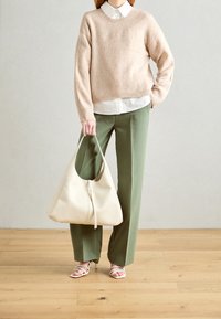 Pull en tricot beige, chemise blanche à col, pantalon large vert olive, sac souple beige clair avec fermeture éclair, et sandales blanches à brides.