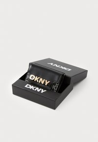 Portafoglio DKNY in materiale sintetico nero, logo dorato sul davanti, design testurizzato, confezionato in una scatola nera con nome del marchio in bianco.