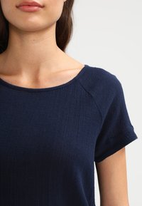 Mörkblå kortärmad tröja med texturerad yta, rund halsringning och upprullade ärmar. Tyget verkar mjukt och lätt.