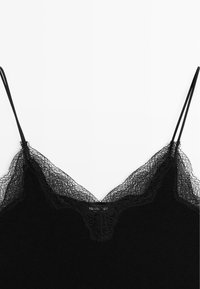 Camisole noire avec une délicate bordure en dentelle le long de l'encolure. Présente des bretelles spaghetti fines et réglables ainsi qu'une texture de tissu douce et côtelée.