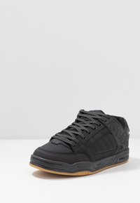 Sneaker basse nere con lacci grigi, contrassegnate con il marchio "GLOBE" sui lati e sul tallone, e suola di colore gomma su una superficie bianca.