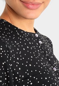 Blusa nera con un motivo a stelle e pois, dotata di colletto arrotondato e bottoni a vista. Il tessuto presenta una texture liscia.