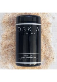 Conteneur cylindrique noir étiqueté "Sels de Lune" entouré de sels de bain himalayens roses, avec des accents argentés et un design moderne.