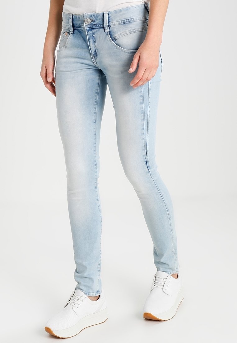 Ljusblå skinny jeans i denim, med en klassisk femfickdesign och subtil blekning, tillsammans med vita sneakers.