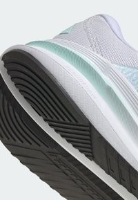 Gros plan de la semelle blanche et menthe d'une chaussure de course avec une bande de roulement noire et une semelle intermédiaire texturée étiquetée "Cloudfoam."