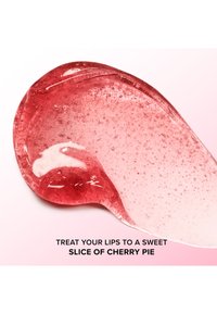 Transparante gel met een glanzende, rode en roze gradient, met kleine luchtbellen, die lijkt op kersen taartvulling. De tekst eronder luidt: "Verwen je lippen met een zoete plak kersentaart."