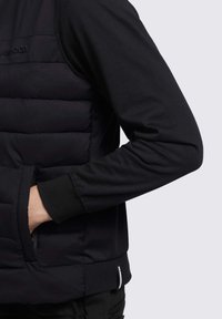 Sort puffer vest med en glat tekstur, som har en lynlåslomme og ribbede manchetter. Beklædningen har et minimalistisk design med en tætsiddende pasform.