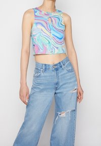 Haut sans manches coupé avec un motif coloré en tourbillon dans des teintes pastel ; présente une découpe en keyhole à l'avant et un ourlet droit. Porté avec un jean léger bleu déchiré.