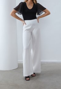 Černý body s průsvitnými krátkými rukávy, kombinovaný s bílé kalhoty širokých nohavic s vysokým pasem a černé sandály s otevřenou špičkou. Jednoduchý a moderní design.