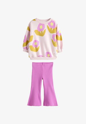 Top de manga larga rosa con estampado floral en amarillo y rosa y etiqueta "Happy Days", combinado con pantalones acampanados rosa sólidos de canalé.