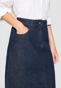 Jeanskjol i mörkblått, med hög midja, sidofickor och en enkel knäppning, samt synliga sömnadsdetaljer.