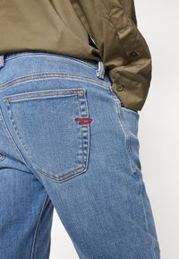 Jeans de mezclilla azul con un corte clásico, que presentan costuras en contraste y un pequeño logo rojo en el bolsillo trasero.