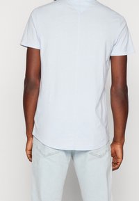 Světle modré tričko s krátkým rukávem a zaobleným lemem. Měkká tkanina, jednoduchý design, jemné švy probíhající vertikálně po zadní straně.