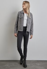 Grå texturerad jacka med krage, framfickor och dragkedjestängning, tillsammans med svarta slim jeans och svarta ankelboots.