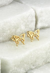 Guldörhängen i form av fjärilar med intrikata detaljer, framträdande vingar och en slät yta, mot en ljus marmorbakgrund.