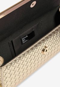 Clutch intessuta in oro con un esterno metallico testurizzato, fodera in tessuto nero e una piccola etichetta interna con il testo "amici come questi."