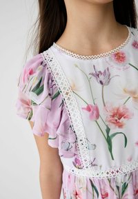 Blumenkleid mit pinken und weißen Blumen, ausgestattet mit rüschigen, transparenten Ärmeln und einem weißen Spitzenbesatz am Ausschnitt und der Empire-Taille.