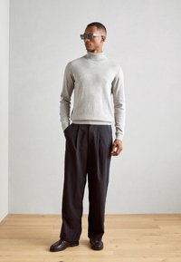 Pulover gri cu guler înalt, realizat dintr-un material moale, asortat cu pantaloni în dungi navy și pantofi din piele negri. Ochelarii de soare pătrați adaugă un contrast.