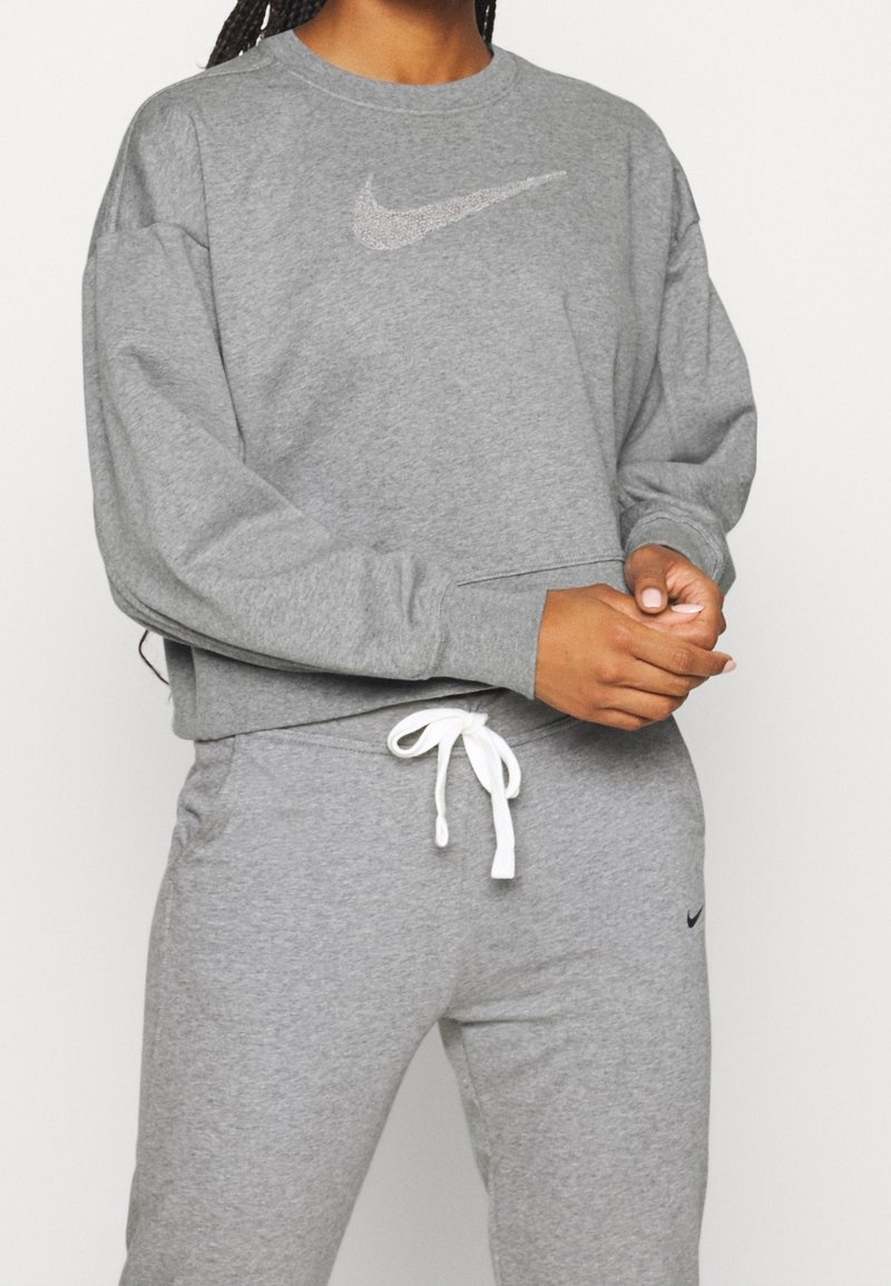 Szara bawełniana bluza z okrągłym dekoltem i długimi rękawami, z metalicznym logo Nike na piersi. W komplecie z szarymi spodniami dresowymi i białymi sznurkami.